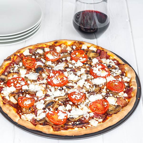 An all-season pizza recipe, featuring a mix of BBQ and pizza sauce, with grilled chicken and bacon, on a thin crust made from scratch, topped with feta cheese.