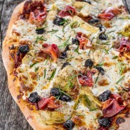 Rustic looking home-made pizza loaded with artichokes, olives and prosciutto