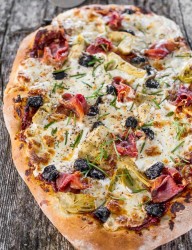 Rustic looking home-made pizza loaded with artichokes, olives and prosciutto