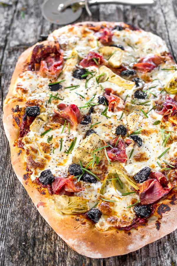 Rustic looking home-made pizza loaded with artichokes, olives and prosciutto